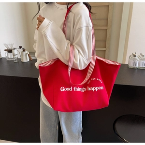 Detail of red canvas tote bag featuring white slogan print and striped shoulder straps
