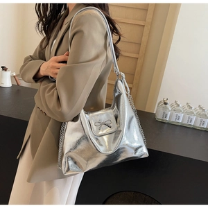 Detail of silver metallic tote bag featuring a bow buckle and chain shoulder strap