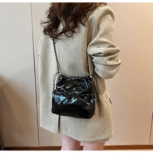 Détail du sac bandoulière en cuir verni noir avec nœud décoratif et bandoulière chaîne