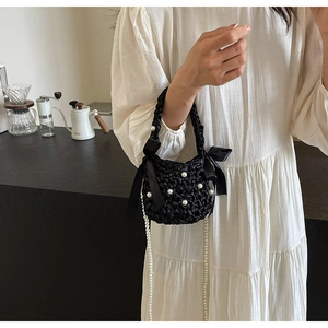 Detail of hand-woven black mini bag featuring white pearls and elegant silk bows