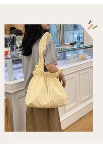 Macro detail of a pale yellow nylon tote bag featuring drawstring closure and ruffled strap