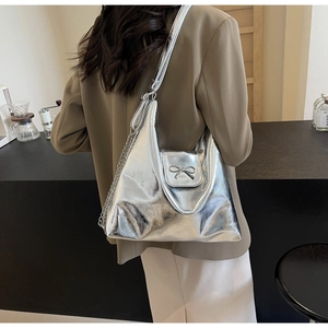 Detail of silver metallic hobo bag with chrome bow decoration and chain strap on shoulder