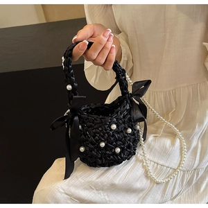 Close-up of black woven bucket bag with pearl embellishments and silk satin bows