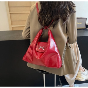 Detailed view of red patent leather handbag with a silver metal bow and chain strap