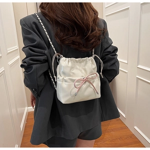 Détail du sac seau en PU blanc crème avec nœuds roses et bandoulière en chaîne
