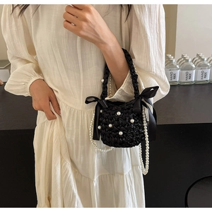 Detail of black woven mini bag with white pearls and silk bows on a pearl crossbody chain