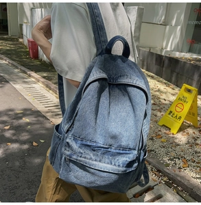Detailed side view of washed blue denim backpack with pockets on an outdoor street background