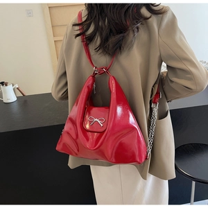 Detail of a bright red PU leather handbag with metal bow and silver chain on a model