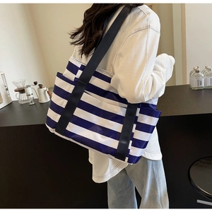 Detail of blue and white striped tote bag with leather strap worn by a model in a cafe