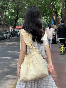 Detail of light yellow sequined tote bag featuring ruffled shoulder straps and drawstring