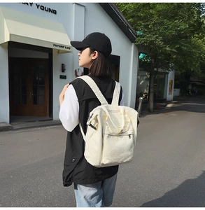 Outdoor street view of a beige canvas backpack with adjustable straps and top handle