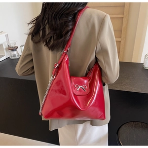 Detail of red faux leather shoulder bag featuring a silver metal bow and chain strap