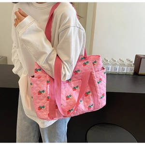 Close-up of pink quilted handbag featuring red strawberry patterns and soft fabric straps