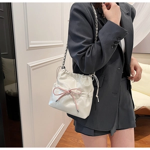 Détail du sac seau en cuir verni blanc avec nœud rose et bandoulière chaîne
