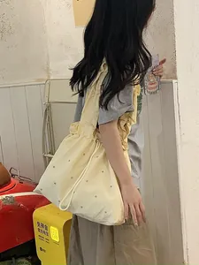 Detail of light yellow nylon tote bag with drawstring closure and ruffled shoulder strap