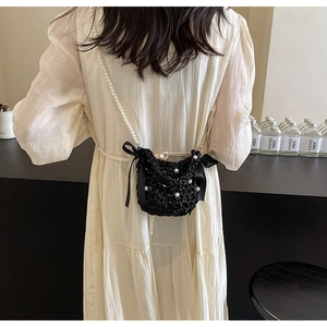 Detail of hand-woven black mini crossbody bag with white pearl beads and satin bows