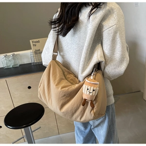 Detail view of khaki crescent nylon bag with a cute coffee cup plush pendant on a model