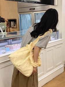 Detail of light yellow ballet style ruffle shoulder bag with metallic eyelets and drawstring