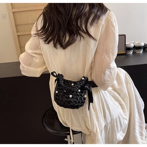 Detail view of black woven crossbody bag with pearls and ribbon bows on model