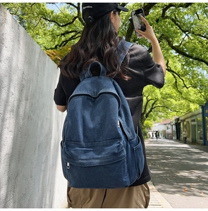 Street style shot of a woman wearing the dark blue denim backpack in a scenic park