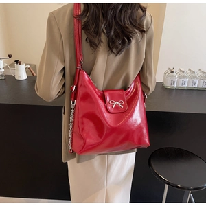 Detail of red glossy shoulder bag with silver bow buckle and chain in cafe setting
