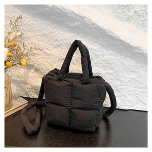 Minimalist black quilted puffer crossbody bag with plush handles and adjustable strap