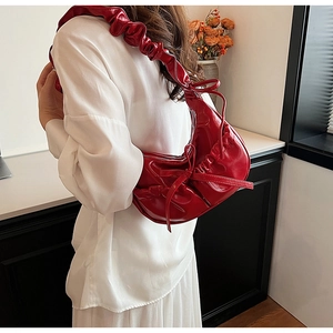 Detail of red pleated PU leather handbag featuring a decorative bow on the shoulder strap