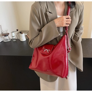Detail of red glossy PU handbag with silver bow accent and metallic chain strap detail