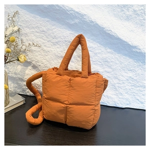 Quilted bright orange puffy tote bag with top handles and adjustable strap on wood table