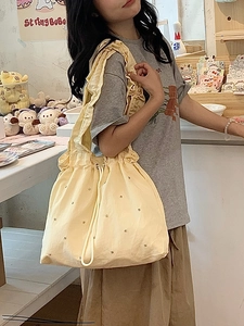 Detail of yellow canvas tote bag featuring ruffled straps and shimmering gold accents
