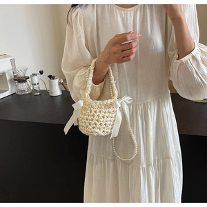 Close-up of elegant cream satin woven bucket bag with pearls and delicate side bow