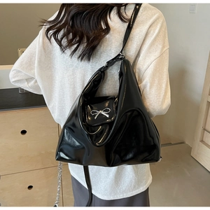 Close-up of black patent leather hobo bag featuring a silver metal bow accent