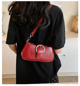 Detail view of a red baguette bag with a large silver horseshoe buckle on a thin shoulder strap