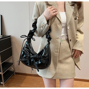 Detail of black glossy PU leather shoulder bag with pleated strap and side bow detail