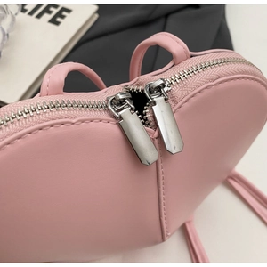 Dettaglio della borsa rosa a forma di cuore con doppie cerniere argentate e trama in pelle