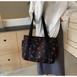 Close-up of black quilted tote bag with red cherry print and wide shoulder straps