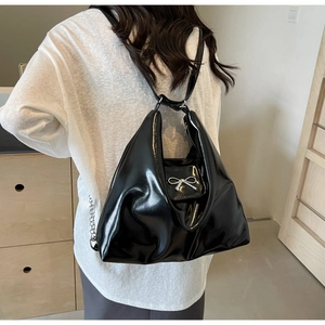 Detail of black glossy PU leather handbag featuring a silver metal bow buckle accent