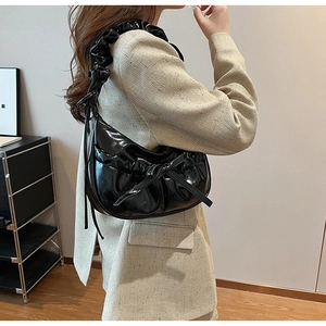 Close-up of black glossy PU leather shoulder bag featuring a decorative bow and pleated strap