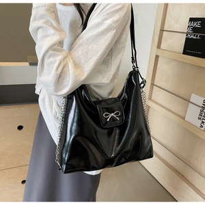 Detail of glossy black PU leather tote bag with silver metallic bow and chain strap accents