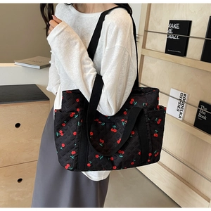 Detail of black quilted tote bag with red cherry print and wide fabric handles
