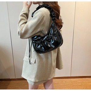 Detail of black faux leather croissant bag with pleated texture and bow decoration