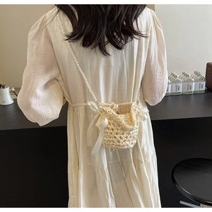 Close-up of handmade cream crochet crossbody bag with ribbon bows and pearl strap worn by model