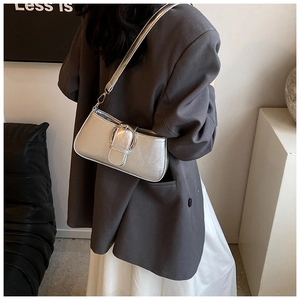 Detail of silver metallic patent leather shoulder bag with large round buckle on model