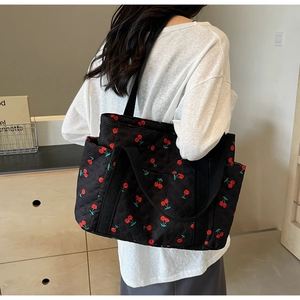 Close-up of black quilted tote bag with red cherry pattern and dual webbed handles