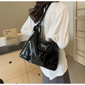 Detail of glossy black patent leather tote with silver bow and metal chain strap