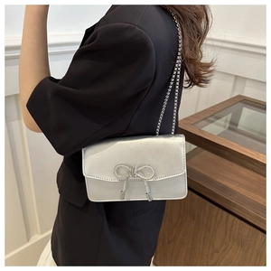 Detail of silver satin evening bag featuring a large sparkling rhinestone bow and chain strap