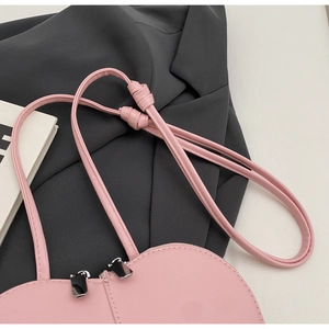 Dettaglio borsa rosa a forma di cuore con doppia zip argentata e tracolla con nodo