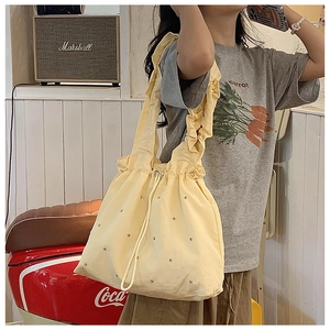 Close-up of light yellow nylon tote bag with ruffle shoulder strap and golden rivet details