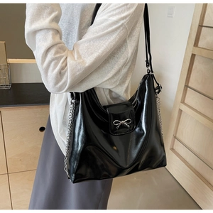 Detail of black patent leather tote bag with silver bow accent and chain on model