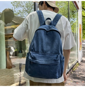 Detail of a dark blue denim backpack featuring wide straps and large zipper pocket on street
